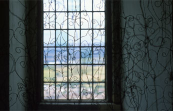 multiple twisted wire drawings of decorative iron fencework hung infront of narrow leaded window of castlecastle